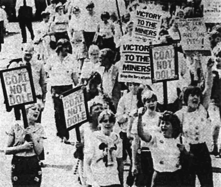 Miners' families marching down street with signs: Victory to the miners; Coal not dole!